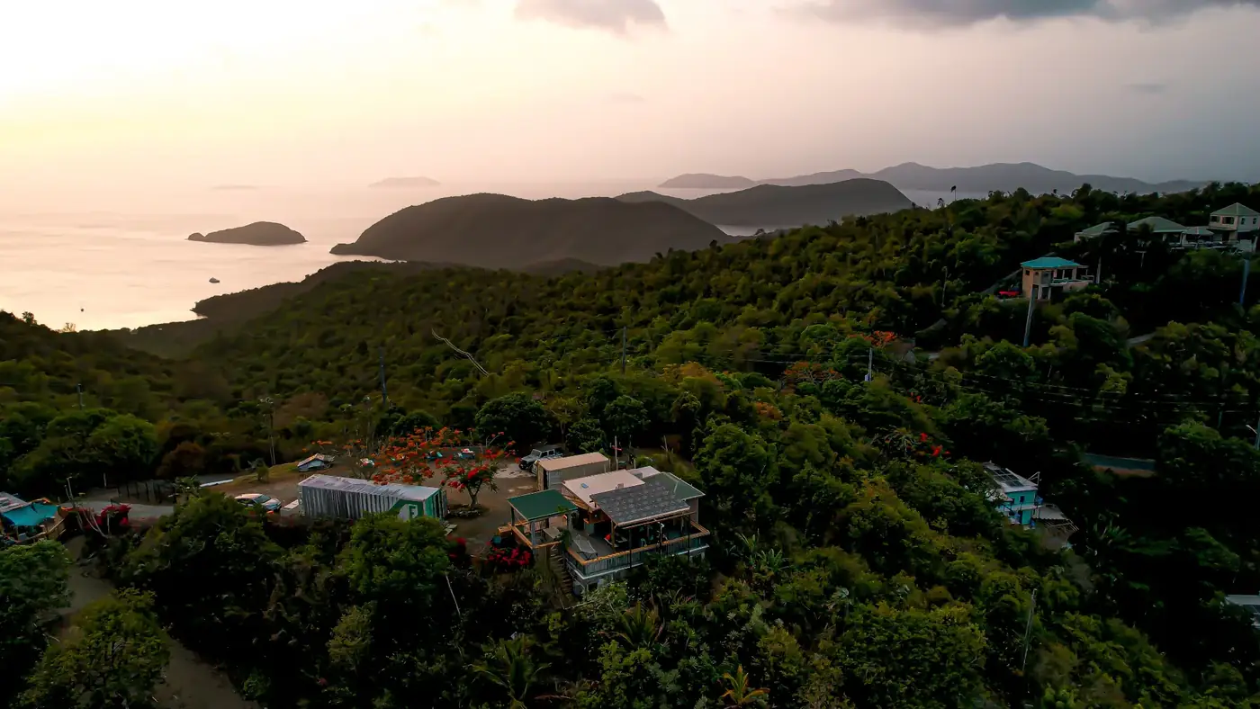Aerial view of Drifters on the St. John hilltop at sunset — lush green ridges, the venue, and Caribbean islands on the horizon